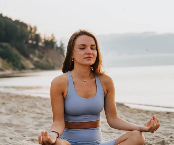 Person meditating peacefully in a natural setting at sunrise.